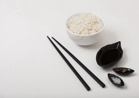White bowl with boiled organic basmati jasmine rice with black chopsticks and sweet soy sauce on white background.の写真素材