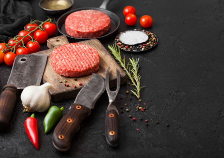 Fresh raw minced homemade farmers grill beef burgers on round chopping board and frying pan with spices and herbs and meat hatchet on black board. Space for textの写真素材