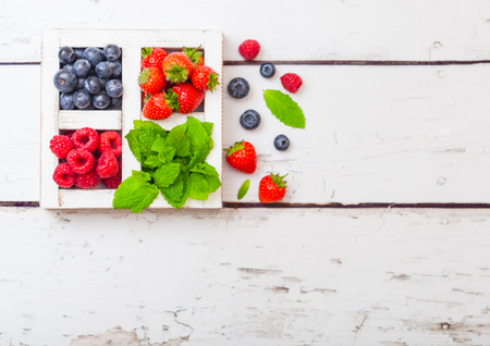 Fresh raw organic berries in white wooden box on wood background. Space for text. Strawberry, Raspberry, Blueberry and Mint leafの写真素材
