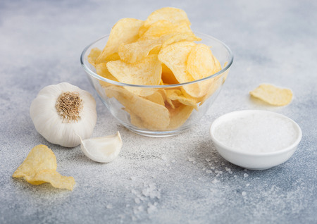 Glass bowl plate with potato crisps chips with onion flavour with garlic and salt on light background.の写真素材