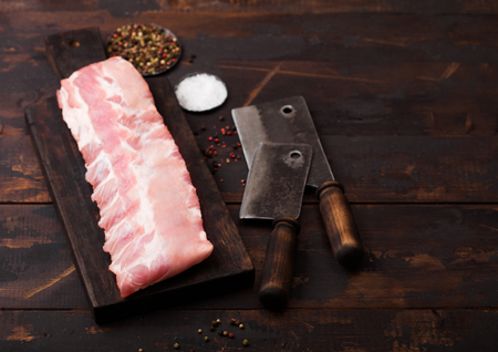Fresh raw pork ribs on chopping board and vintage hatchets on wooden background. Pepper and salt.の写真素材