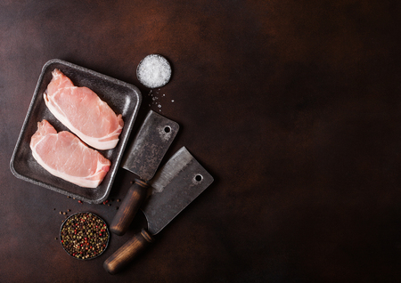 Raw pork loin chops in plastic tray with salt and pepper and vintage meat hatchets on rusty background.の写真素材
