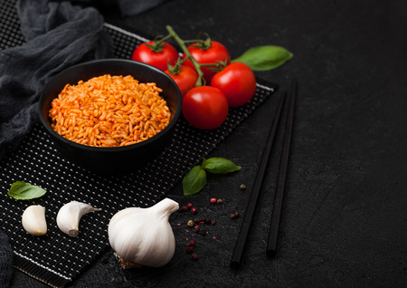 Black plate bowl of rice with tomato and basil and garlic and chopsticks on black background. の写真素材
