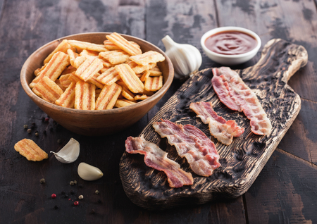 Bacon flavoured snacks with grilled bacon rashers on vintage chopping board with garlic and sauce on wood background.の写真素材