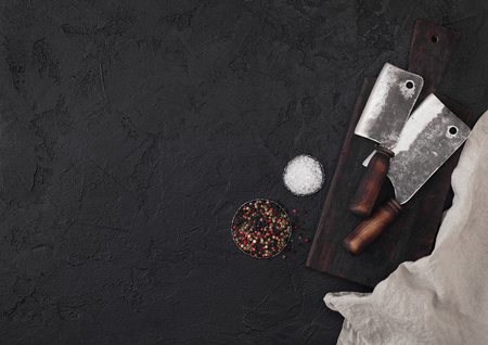 Vintage meat knife hatchet on vintage chopping board and black stone table background. Butcher utensils. Space for textの写真素材