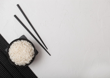 White bowl with boiled organic basmati jasmine rice with black chopsticks on bamboo place mat on white background.の写真素材