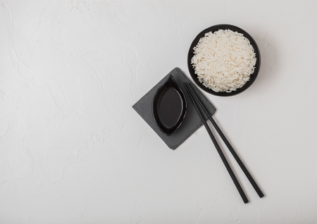 Black bowl with boiled organic basmati jasmine rice with black chopsticks and sweet soy sauce on stone mat on white.の写真素材