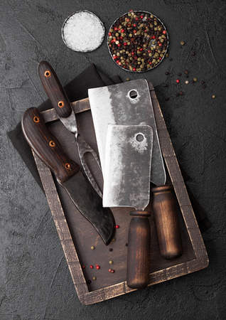 Vintage meat knife and fork and hatchet in old wooden box on black table background. Butcher utensils.の写真素材