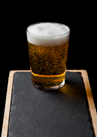 Glass of lager beer with foam and bubbles on stone board on black.の写真素材