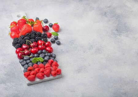 Fresh organic summer berries mix on white marble board on light kitchen table background. Raspberries, strawberries, blueberries, blackberries and cherries. Top viewの写真素材