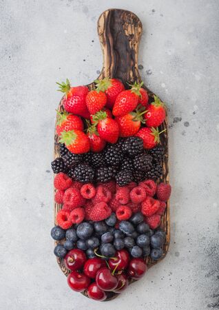 Fresh organic summer berries mix on vintage wooden chopping board on light kitchen table background. Raspberries, strawberries, blueberries, blackberries and cherries. Top viewの写真素材