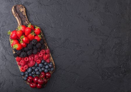 Fresh organic summer berries mix on vintage wooden chopping board black table background. Raspberries, strawberries, blueberries, blackberries and cherries.Top viewの写真素材