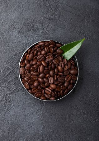 Fresh raw organic coffee beans in steel bowl with coffee trea leaf on black.の写真素材