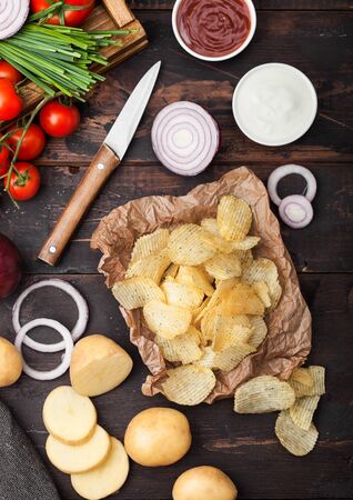 Fresh organic homemade potato crisps chips with sour cream and red onions on paper on wooden background.の写真素材