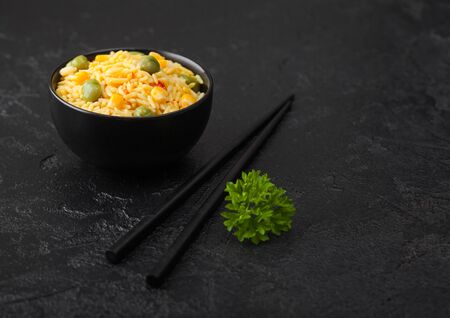Whi Black bowl with boiled organic basmati vegetable rice with black chopsticks on black background. Yellow corn and green peas with paprika slices.の写真素材