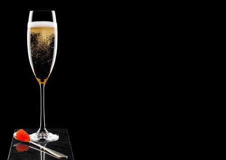 Elegant glass of yellow champagne with red caviar on golden spoon of caviar on marble board on black.の写真素材