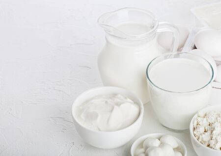 Fresh dairy products on white table background. Jar and glass of milk, bowl of sour cream, cottage cheese and mozzarella. Eggs in wooden box. Space for textの写真素材