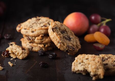 Homemade organic oatmeal cookies with raisins and apricots on dark wood background with apricot and grapes.の写真素材