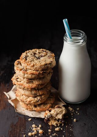 Homemade organic oatmeal cookies with raisins and apricots and bottle of milk on dark wood background.の写真素材