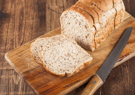 Cut of fresh loaf of seeded bread on wooden background with chopping board and bread knife....