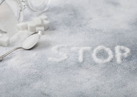 Glass jar of natural white refined sugar with cubes with silver spoon on light background with STOp letters. Unhealthy food concept.の写真素材