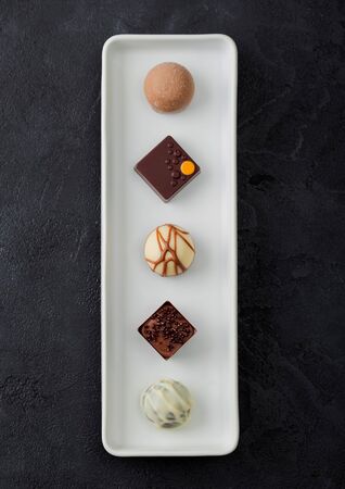 Luxury Chocolate candies selection in white porcelain plate on black background.White, dark and milk chocolate assortment. Top viewの写真素材