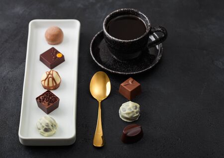 Luxury Chocolate candies in white porcelain plate with cup of black coffee and golden spoon on dark background. Top viewの写真素材