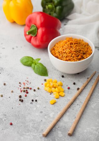 White ceramic bowl plate with boiled red long grain basmati rice with vegetables on light background with sticks and paprika pepper with corn,garlic and basil.の写真素材