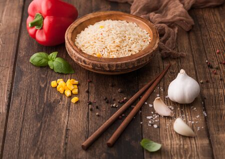 Wooden bowl with boiled long grain basmati rice with vegetables on wooden table background with sticks and red paprika with corn,garlic and basil.の写真素材