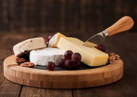 Selection of various cheese on the board and grapes on wooden table background. Blue Stilton, Red Leicester and Brie Cheese with knife on round chopping board.の写真素材