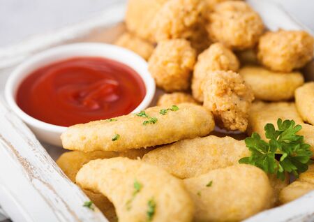 Buttered chicken nuggets and popcorn bites in white vintage wooden box with ketchup on light...
