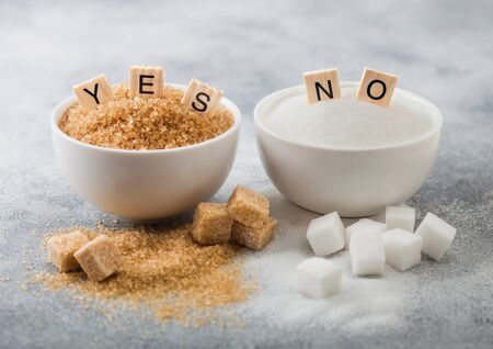 White bowl plates of natural brown and white refined sugar and cubes on light background.Yes and no letters. Healthy and unhealthy concept.の写真素材