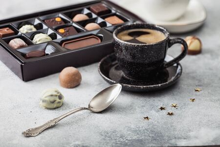 Box of Luxury Chocolate candies selection with cup of black coffee and silver spoon on light...