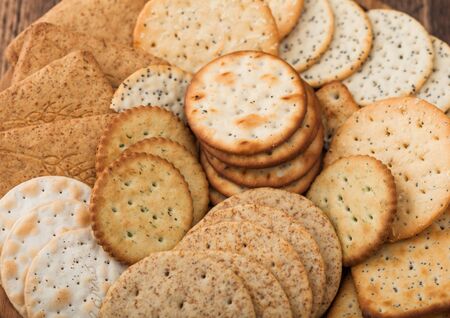 Various organic crispy wheat, rye and corn flatbread crackers with sesame and salt in round plate on wood background.の写真素材