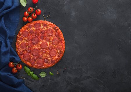 Fresh round baked Hot and Spicy Pepperoni pizza with tomatoes with basil on black kitchen table background.の写真素材