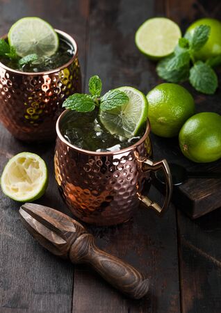 Moscow mule cocktail in a copper mug with lime and mint and wooden squeezer on dark wooden table background.の写真素材