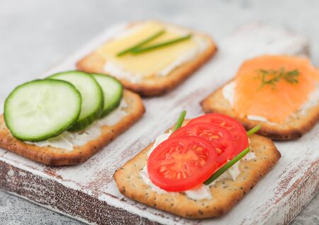 Various healthy crackers with salmon and cheese, tomato and cucumber on wooden chopping board on light table background. Top viewの写真素材