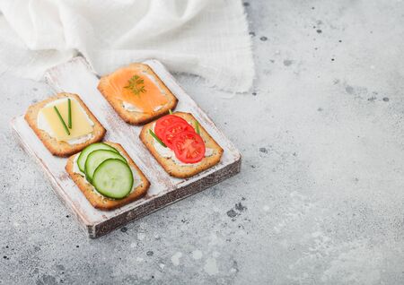 Various healthy crackers with salmon and cheese, tomato and cucumber on wooden chopping board on light table background. Top viewの写真素材