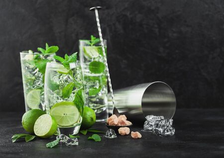 Luxury Glasses of Mojito cocktail with ice cubes mint and lime on black board with spoon and fresh limes with cane sugar and steel shaker. Best summer cocktail.の写真素材