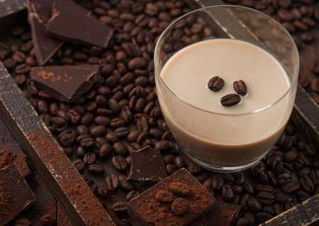 Irish cream baileys liqueur in glass with coffee beans and powder with dark chocolate in wooden tray...