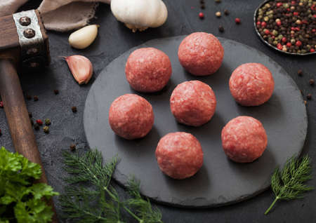 Raw fresh minced beef meatballs on round board with pepper, garlic and parsley on black table background.の写真素材