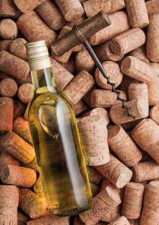 Bottle of white wine and vintage corkscrew on top of various wine corks background.の写真素材