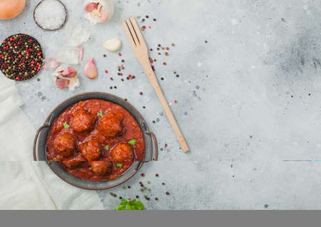 Traditional spicy meatballs in tomato sauce with pepper, garlic and parsley on light table with utensils. Space for textの写真素材