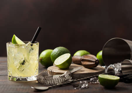 Gimlet Kamikaze cocktail in crystal glass with lime slice and ice on wooden background with fresh limes and strainer with shaker.の写真素材