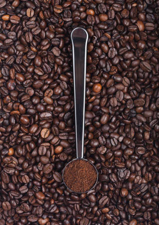 Fresh raw organic coffee powder in silver steel scoop on top of coffee beans. Top viewの写真素材