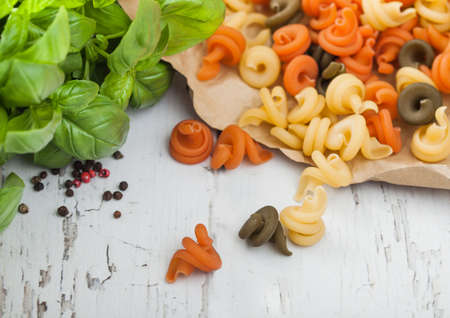 Raw homemade tricolore trottole pasta in brown paper on white wooden table background with basil.の写真素材