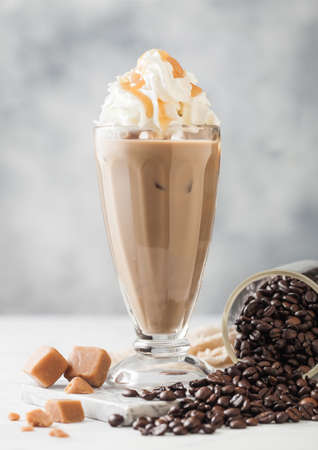 Black iced coffee with fresh milk and caramel with cream in classic milkshake glass and jar of raw...