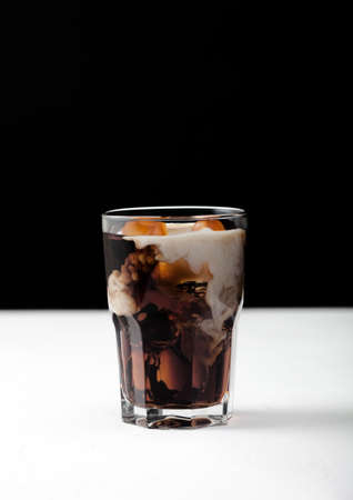 Glass of black coffee with ice cubes and fresh milk on white board and black background.の写真素材