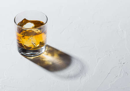 Glass with ice cubes of single malt whiskey on white background with deep shadow.