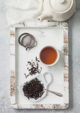 Black loose tea with tea ball strainer infuser and ceramic teapot with cup in wooden box with white...